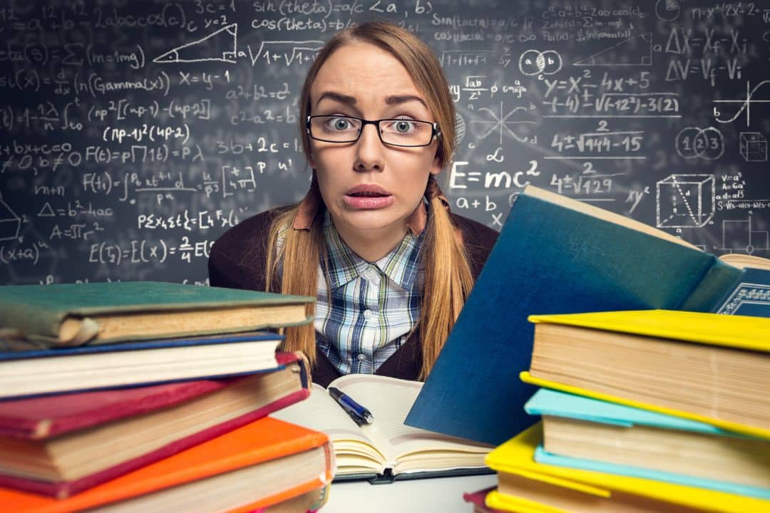 Studentka w okularach wśród książek na tle tablicy